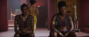 Movie still from “The Woman King” (2022), directed by Gina Prince-Bythewood – A couple of women sitting next to each other in a room; Medium shot, Over the shoulder angle