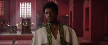 Movie still from “The Woman King” (2022), directed by Gina Prince-Bythewood – A man in a white robe standing next to a red wall; Medium shot, Over the shoulder angle