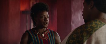 Movie still from “The Woman King” (2022), directed by Gina Prince-Bythewood – A black woman with a colorful striped shirt and necklace; Close Up shot, Over the shoulder angle