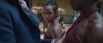 Movie still from “The Woman King” (2022), directed by Gina Prince-Bythewood – A young woman with a braid is looking into the camera; Close Up shot, Over the shoulder angle