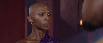 Movie still from “The Woman King” (2022), directed by Gina Prince-Bythewood – A bald woman with a purple shirt and a purple and white pattern shirt; Close Up shot, Low angle