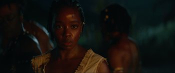 Movie still from “The Woman King” (2022), directed by Gina Prince-Bythewood – A young woman with a yellow necklace and a man in a black suit; Close Up shot, Over the shoulder angle
