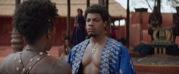 Movie still from “The Woman King” (2022), directed by Gina Prince-Bythewood – A man in a blue and gold jacket looking at a woman in a blue and gold jacket; Close Up shot, Over the shoulder angle