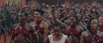 Movie still from “The Woman King” (2022), directed by Gina Prince-Bythewood – A group of people are standing in a crowd and raising their fists in the air; Medium shot, Low angle
