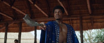 Movie still from “The Woman King” (2022), directed by Gina Prince-Bythewood – A man in a blue robe holding a knife; Medium shot, Low angle
