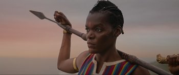 Movie still from “The Woman King” (2022), directed by Gina Prince-Bythewood – A woman holding a wooden stick with a face painted on it; Close Up shot, Low angle