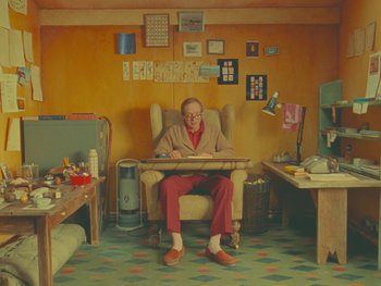 Movie still from “The Wonderful Story of Henry Sugar” (2023), directed by Wes Anderson – An older man sitting in a chair in a room; Wide shot, High angle