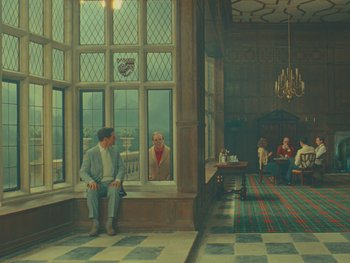 Movie still from “The Wonderful Story of Henry Sugar” (2023), directed by Wes Anderson – A man sitting on a window ledge looking out a window; Extreme Wide shot, Over the shoulder angle