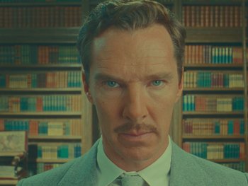 Movie still from “The Wonderful Story of Henry Sugar” (2023), directed by Wes Anderson – A man in a suit standing in front of a book shelf; Close Up shot, Low angle