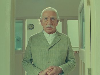 Movie still from “The Wonderful Story of Henry Sugar” (2023), directed by Wes Anderson – An old man in a suit standing in front of a door; Medium shot, Low angle