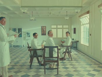 Movie still from “The Wonderful Story of Henry Sugar” (2023), directed by Wes Anderson – A group of men sitting at a table in front of a window; Wide shot, Low angle