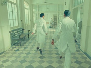 Movie still from “The Wonderful Story of Henry Sugar” (2023), directed by Wes Anderson – Two men in white lab coats walking in a room; Wide shot, High angle