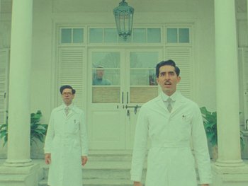 Movie still from “The Wonderful Story of Henry Sugar” (2023), directed by Wes Anderson – Two men in white lab coats standing in front of a building; Wide shot, Low angle
