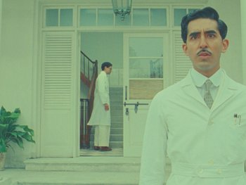 Movie still from “The Wonderful Story of Henry Sugar” (2023), directed by Wes Anderson – A man standing in front of a door with another man standing in front of it; Medium shot, Low angle