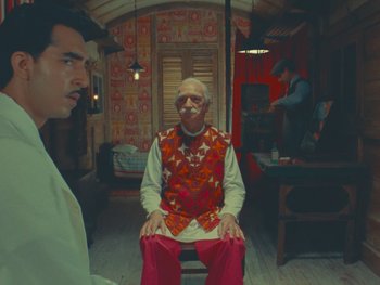 Movie still from “The Wonderful Story of Henry Sugar” (2023), directed by Wes Anderson – A man sitting on a chair in front of another man in a room; Wide shot, Low angle