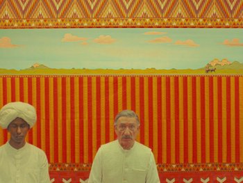 Movie still from “The Wonderful Story of Henry Sugar” (2023), directed by Wes Anderson – Two men standing in front of a red wall; Wide shot, Low angle