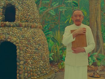 Movie still from “The Wonderful Story of Henry Sugar” (2023), directed by Wes Anderson – An old man holding a bag in front of a stone wall; Medium shot, Low angle