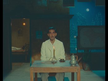Movie still from “The Wonderful Story of Henry Sugar” (2023), directed by Wes Anderson – A man sitting at a wooden table with a candle; Wide shot, High angle
