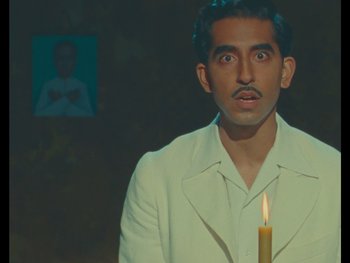 Movie still from “The Wonderful Story of Henry Sugar” (2023), directed by Wes Anderson – A man in a white jacket holding a lit candle; Close Up shot, High angle