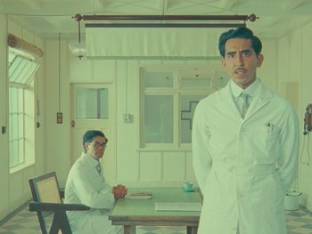 Movie still from “The Wonderful Story of Henry Sugar” (2023), directed by Wes Anderson – Two men in white lab coats standing next to a table; Medium shot, Low angle