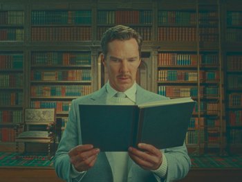 Movie still from “The Wonderful Story of Henry Sugar” (2023), directed by Wes Anderson – A man in a suit and tie holding a book; Medium shot, Low angle