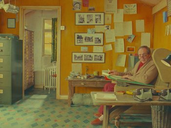 Movie still from “The Wonderful Story of Henry Sugar” (2023), directed by Wes Anderson – An older woman sitting at a table in front of papers; Wide shot, High angle