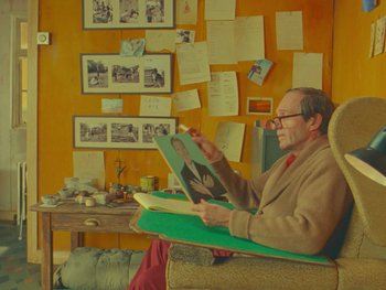 Movie still from “The Wonderful Story of Henry Sugar” (2023), directed by Wes Anderson – An older man sitting in a chair reading a book; Medium shot, High angle