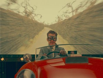 Movie still from “The Wonderful Story of Henry Sugar” (2023), directed by Wes Anderson – A man driving a red car down a street; Medium shot, Low angle