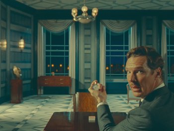 Movie still from “The Wonderful Story of Henry Sugar” (2023), directed by Wes Anderson – A man sitting at a dining table holding a cell phone; Medium shot, Over the shoulder angle