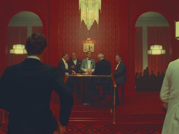 Movie still from “The Wonderful Story of Henry Sugar” (2023), directed by Wes Anderson – A group of men in suits sitting at a dinner table; Wide shot, Over the shoulder angle