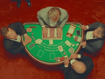Movie still from “The Wonderful Story of Henry Sugar” (2023), directed by Wes Anderson – A group of men sitting around a table playing a game of blackjack; Wide shot, Overhead angle