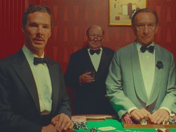 Movie still from “The Wonderful Story of Henry Sugar” (2023), directed by Wes Anderson – Three men in tuxedos standing around a table; Medium shot, Over the shoulder angle