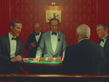 Movie still from “The Wonderful Story of Henry Sugar” (2023), directed by Wes Anderson – A group of men standing around a game table; Medium shot, Over the shoulder angle