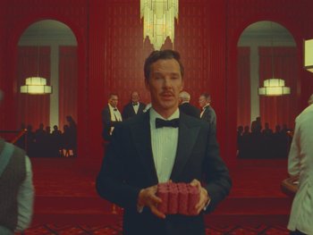 Movie still from “The Wonderful Story of Henry Sugar” (2023), directed by Wes Anderson – A man in a tuxedo holding a box in front of a crowd of people; Medium shot, Low angle