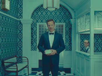 Movie still from “The Wonderful Story of Henry Sugar” (2023), directed by Wes Anderson – A man in a suit and bow tie holding a box; Wide shot, Low angle