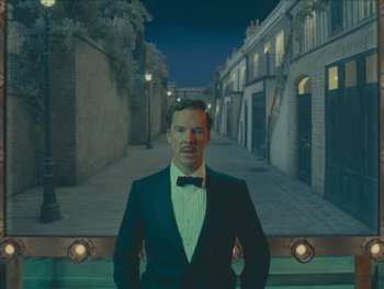 Movie still from “The Wonderful Story of Henry Sugar” (2023), directed by Wes Anderson – A man in a suit and bow tie standing in front of some buildings; Medium shot, High angle