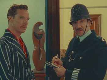 Movie still from “The Wonderful Story of Henry Sugar” (2023), directed by Wes Anderson – A man in a police uniform writing on a piece of paper next to another man; Medium shot, Over the shoulder angle