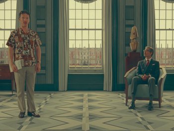 Movie still from “The Wonderful Story of Henry Sugar” (2023), directed by Wes Anderson – A man standing in front of another man sitting in a chair in front of a window; Wide shot, Over the shoulder angle