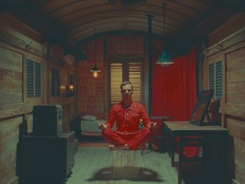 Movie still from “The Wonderful Story of Henry Sugar” (2023), directed by Wes Anderson – A man sitting in a chair in a room with red curtains; Wide shot, Low angle