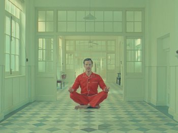 Movie still from “The Wonderful Story of Henry Sugar” (2023), directed by Wes Anderson – A man in red pajamas sitting on the floor in front of a window; Wide shot, Overhead angle