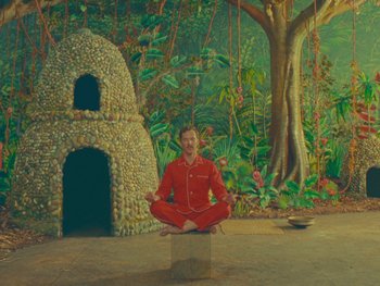 Movie still from “The Wonderful Story of Henry Sugar” (2023), directed by Wes Anderson – A man in a red suit meditates in front of a stone structure; Wide shot, High angle