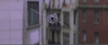 Movie still from “The World Is Not Enough” (1999), directed by Michael Apted – A bullet hole in the window of an apartment building; Extreme Close Up shot, High angle