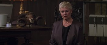 Movie still from “The World Is Not Enough” (1999), directed by Michael Apted – An older woman with short blonde hair wearing a black shirt; Medium shot, Low angle