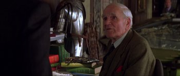 Movie still from “The World Is Not Enough” (1999), directed by Michael Apted – An older man sitting in front of a stack of books; Close Up shot, High angle
