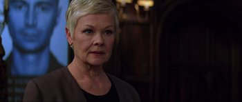 Movie still from “The World Is Not Enough” (1999), directed by Michael Apted – An older woman with short blonde hair wearing a black shirt; Close Up shot, Low angle