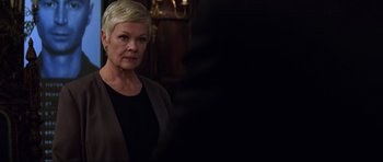 Movie still from “The World Is Not Enough” (1999), directed by Michael Apted – A woman with blonde hair and a black shirt is standing in front of a mirror; Close Up shot, Over the shoulder angle