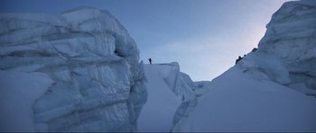 Movie still from “The World Is Not Enough” (1999), directed by Michael Apted – A person is standing on the side of a snow covered mountain; Extreme Wide shot, Low angle