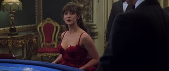 Movie still from “The World Is Not Enough” (1999), directed by Michael Apted – A woman in a red dress sitting in front of a blue table; Medium shot, Over the shoulder angle