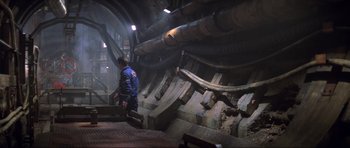 Movie still from “The World Is Not Enough” (1999), directed by Michael Apted – A man in a blue jacket is walking in a tunnel; Wide shot, High angle