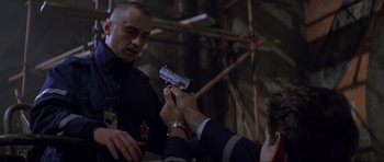 Movie still from “The World Is Not Enough” (1999), directed by Michael Apted – A man holding a gun in his hand while another man looks on; Close Up shot, Low angle
